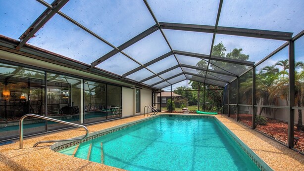 Una piscina interna con struttura in vetro, circondata da un solarium con rivestimento in ciottoli e da una zona patio coperta.
