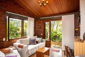 Una sala de estar acogedora con pared de ladrillo, techo de madera y ventanas amplias que dan a vistas de follaje.