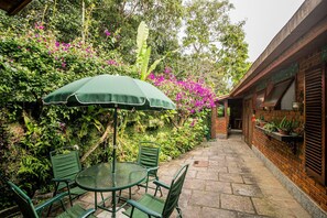 Un patio al aire libre con una mesa redonda y sillas, un paraguas verde y un muro de ladrillo con plantas en macetas.
