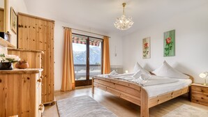 Une chambre à coucher avec un lit en bois, une commode en bois, une grande fenêtre avec des rideaux et un lustre.