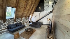 Ein geräumiges Loft mit Steinwand, Holzbalken, einer Treppe und einer modernen Wohnbereich mit Sofas und einem Couchtisch.