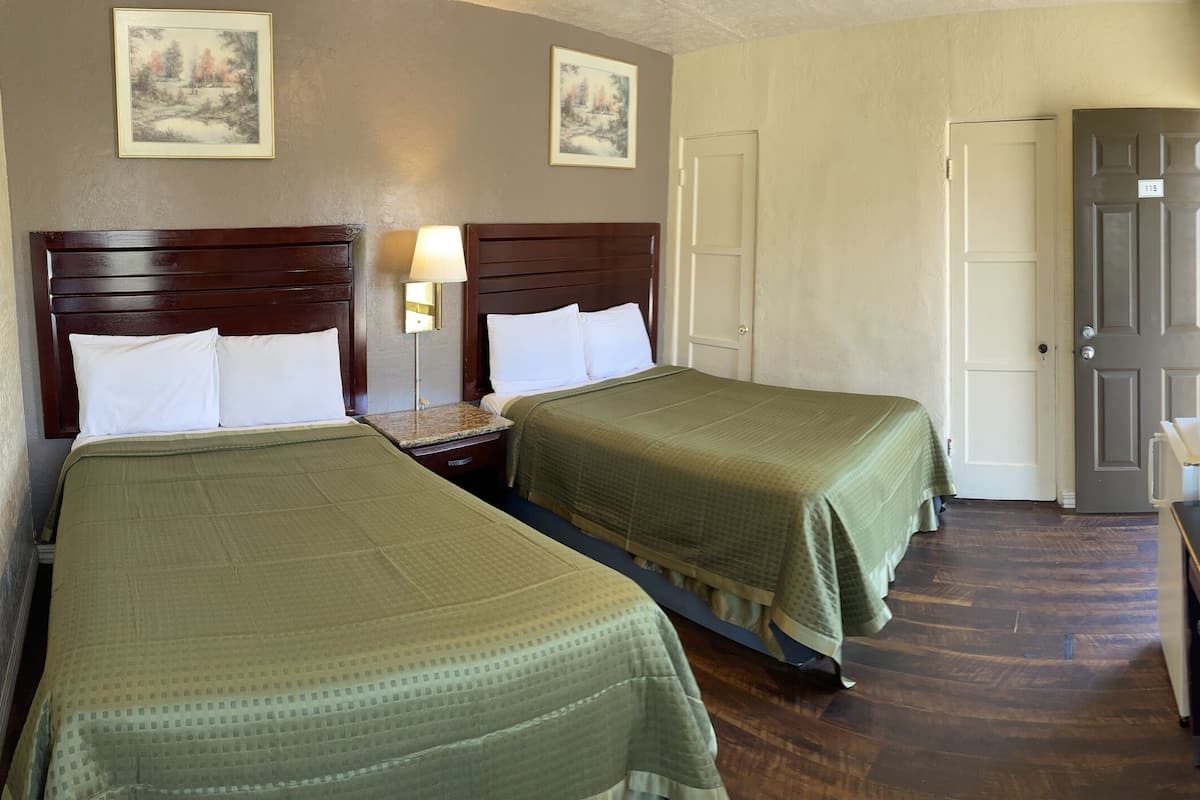 Ein Hotelzimmer mit zwei Einzelbetten, einem Schreibtisch mit Fernseher, einem Spiegel und einer Tür zu einem weiteren Raum.