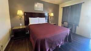 Une chambre d’hôtel avec un grand lit, deux tables de chevet avec des lampes, une tête de lit, un tableau au mur et une fenêtre avec des rideaux.