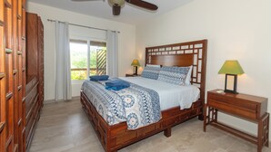 A bedroom with a wooden bed, a ceiling fan, a nightstand with a lamp, and a view of the outdoors through a window. - 2 Bedroom Waterfront Retreat w/ Dock Close to Dining, Diving, and Westend (West End)