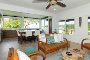 A spacious living area with a sofa, chairs, a dining table, and a ceiling fan.