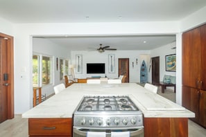A kitchen with a large island, stove, and oven, with a ceiling fan and artwork on the walls.
