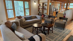 A cozy living room with a sofa, chairs, a coffee table, and a kitchen area with wooden cabinets and a refrigerator. - Meadow Rue Retreat @ Brickyard Creek (Bayfield)