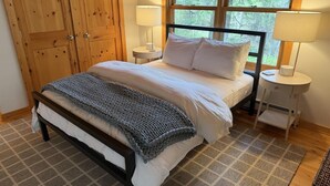 A bedroom with a bed, bedside tables, a lamp, a window, and a wooden wardrobe. - Meadow Rue Retreat @ Brickyard Creek (Bayfield)