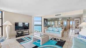 A spacious living room with a large TV, a sofa, a coffee table, and a view of the ocean. - Lighthouse Towers - 1808 (Clearwater)