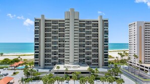 A high-rise hotel with multiple floors, a central atrium, and a parking area with palm trees. - Lighthouse Towers - 1808 (Clearwater)