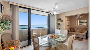A modern living room with a glass table, wicker chairs, a sofa, and a ceiling fan. - Lighthouse Towers - 1808 (Clearwater)