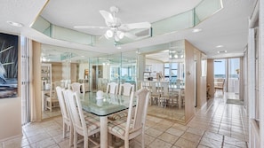 A modern dining area with a glass table, wicker chairs, and a ceiling fan. - Lighthouse Towers - 1808 (Clearwater)