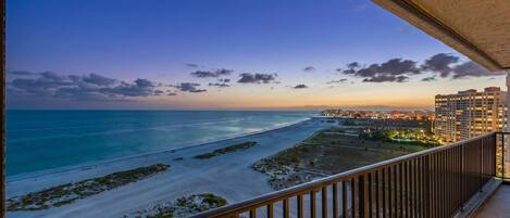 A balcony with a view of a beach and cityscape at dusk.