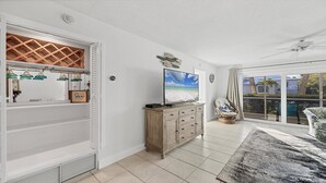 Ein geräumiges Wohnzimmer mit großem Fenster, einem Holzkabinett und einem Deckenventilator.
