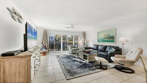 Ein Wohnzimmer mit Flachbildfernseher, einer Couch, einem Sessel, einem Couchtisch und einem Deckenventilator.