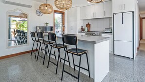 A modern kitchen with a central island, bar stools, a refrigerator, and pendant lights. - Summer Palms - Tairua Holiday Home (Tairua)