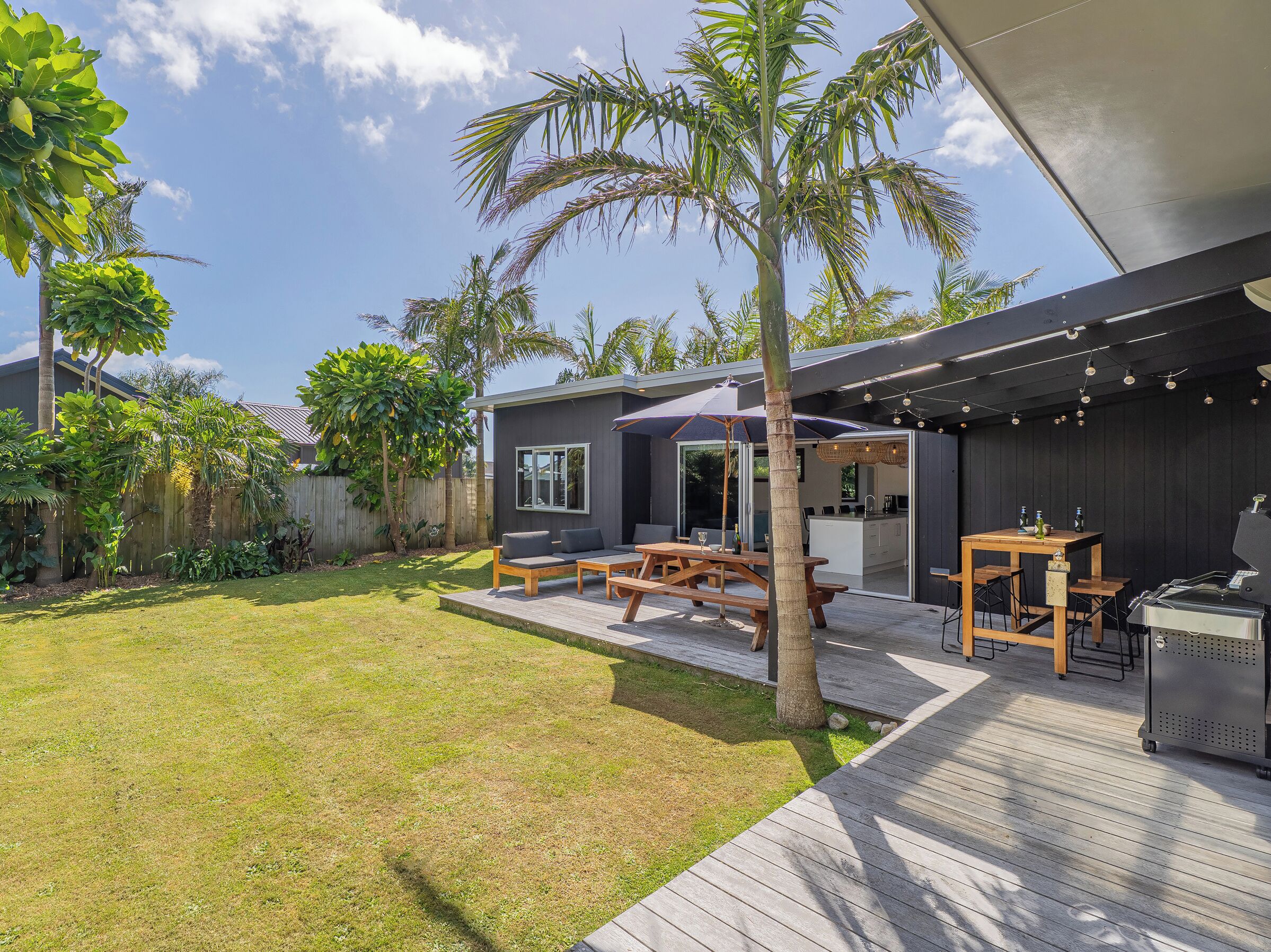 A modern outdoor patio with a wooden deck, a barbecue grill, and a seating area with a table and chairs.
