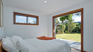 A bedroom with a bed, a window, and a view of a garden. - Summer Palms - Tairua Holiday Home (Tairua)