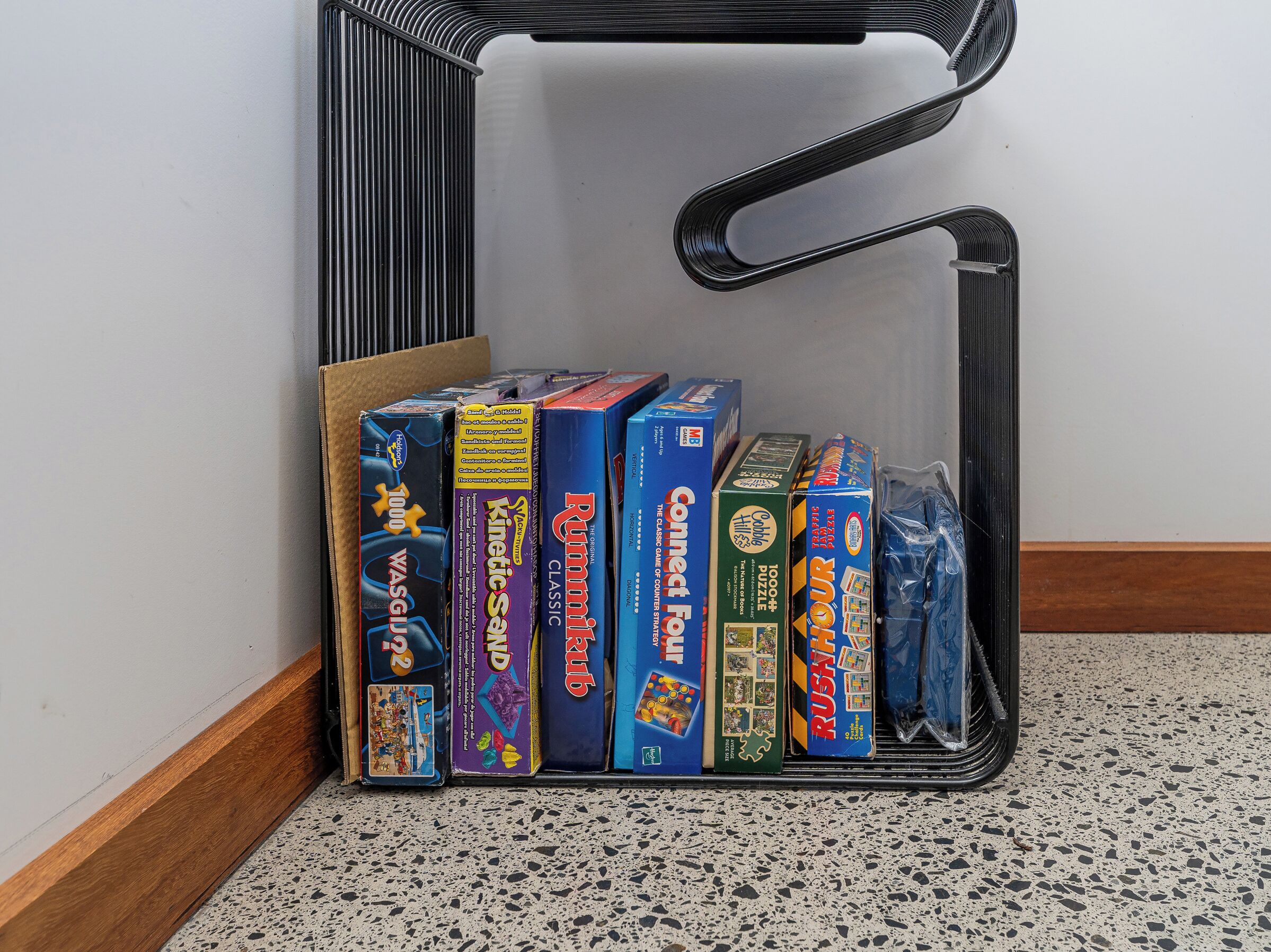 A corner of a room with a black metal shelf holding various board games.