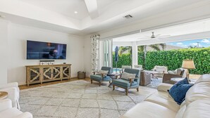 Ein geräumiges Wohnzimmer mit Flachbildfernseher, einer großen Couch und einem Essbereich mit Gartenmöbeln.
