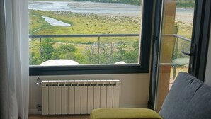 Une pièce dotée d’une grande fenêtre donnant sur un paysage montagneux, d’un radiateur et d’un banc vert rembourré.