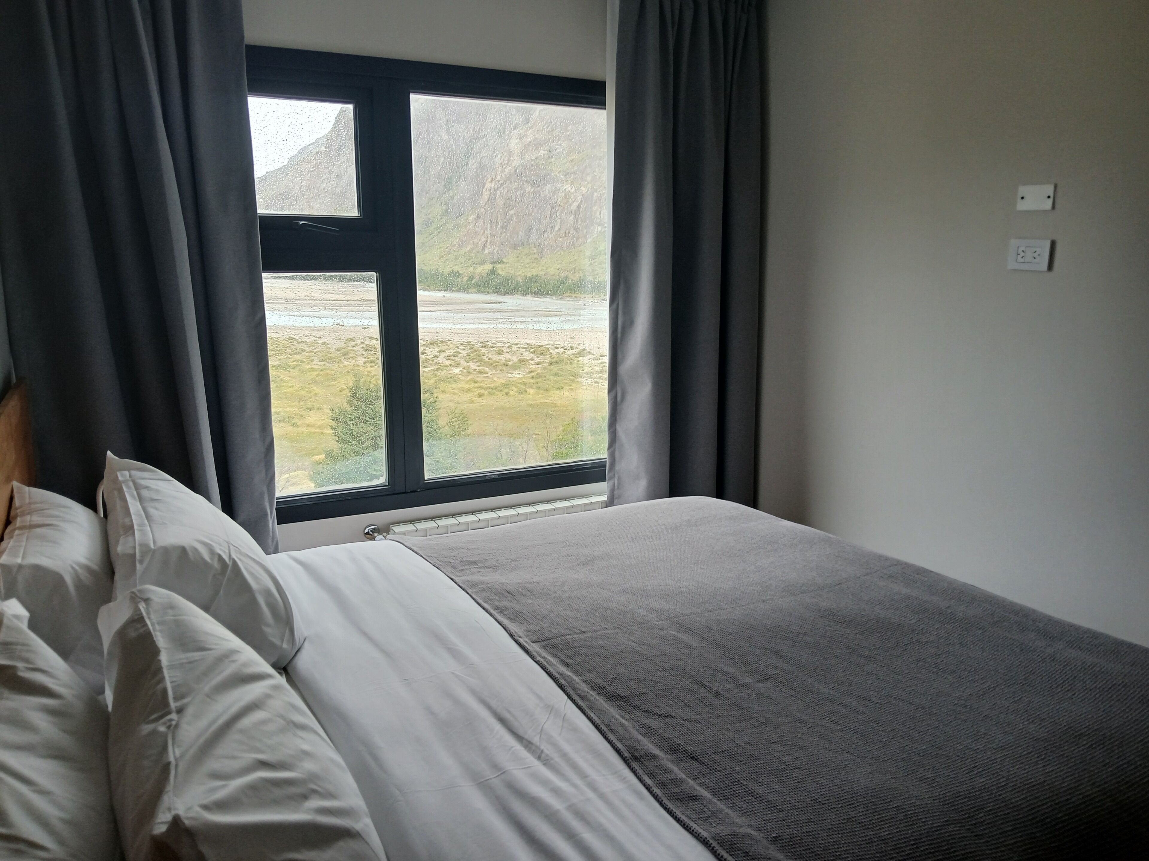 Un dormitorio con cama, ventana con cortinas y vistas al paisaje.