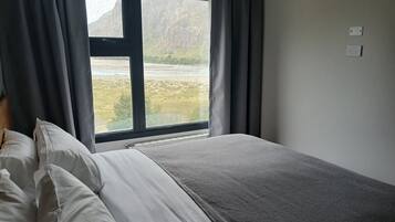 Un dormitorio con cama, ventana con cortinas y vistas al paisaje.