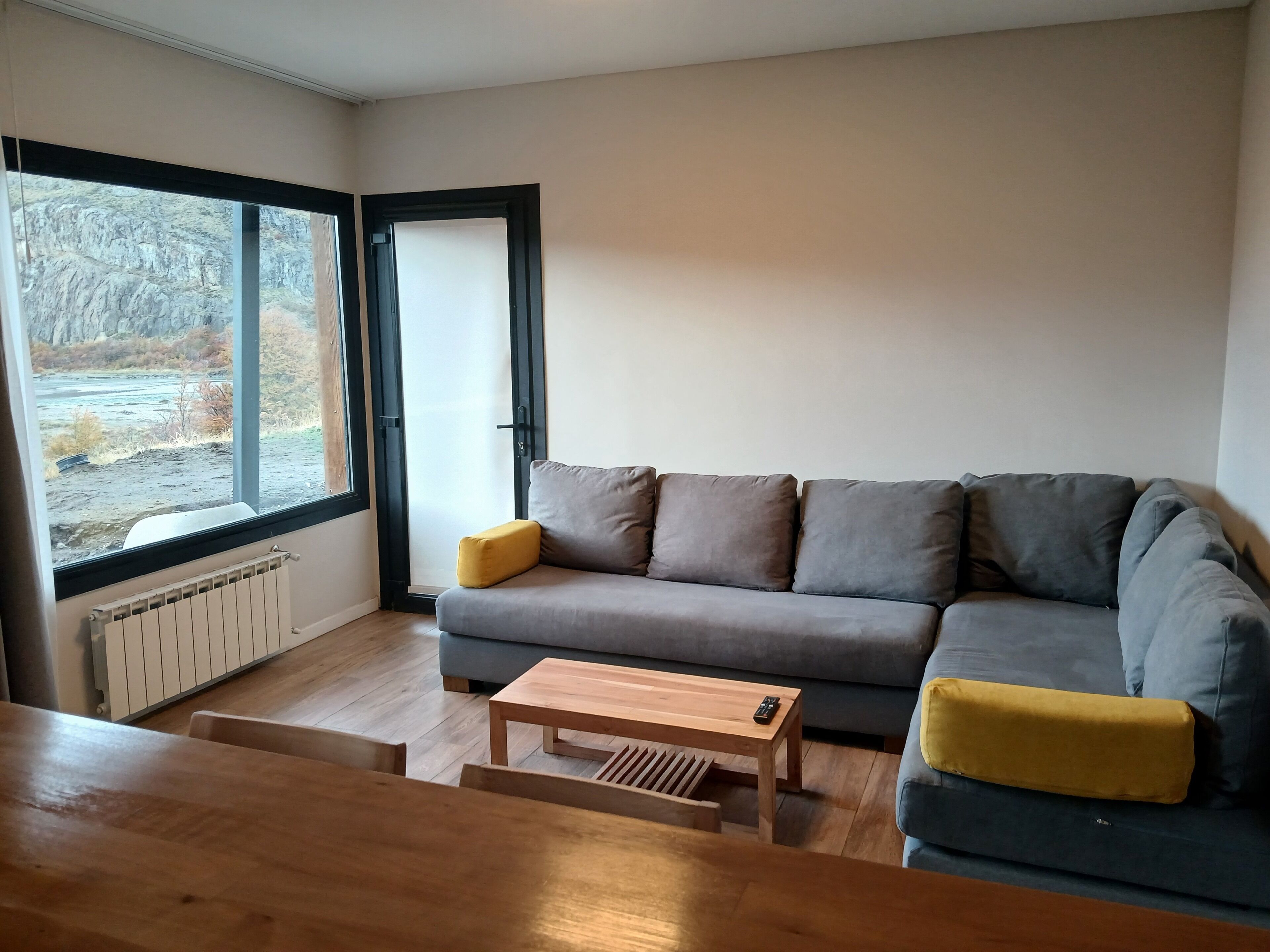 A living room with a grey sofa, a wooden coffee table, and a view through a large window.