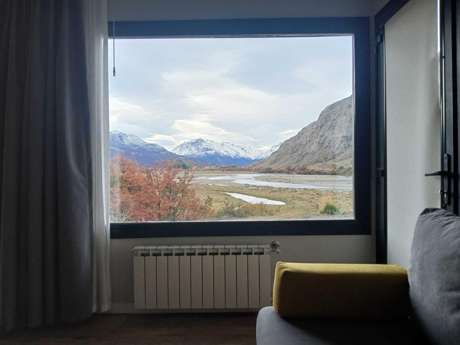 Una habitación con un ventanal que ofrece vistas a un río, montañas y follaje otoñal.