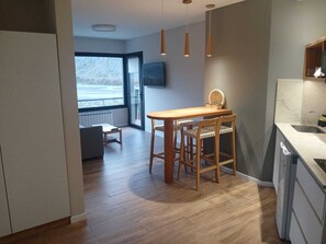 Une cuisine moderne avec une table en bois et des tabourets de bar, une grande fenêtre offrant une belle vue et un éclairage suspendu.