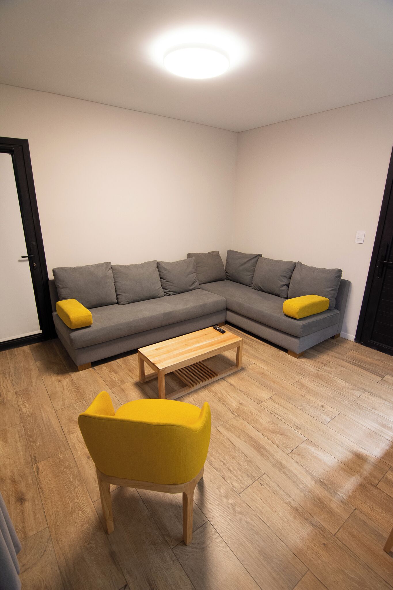 Una sala moderna con un sofá modular gris, un sillón amarillo y una mesa de centro de madera.
