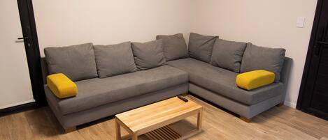 Una sala moderna con un sofá modular gris, un sillón amarillo y una mesa de centro de madera.