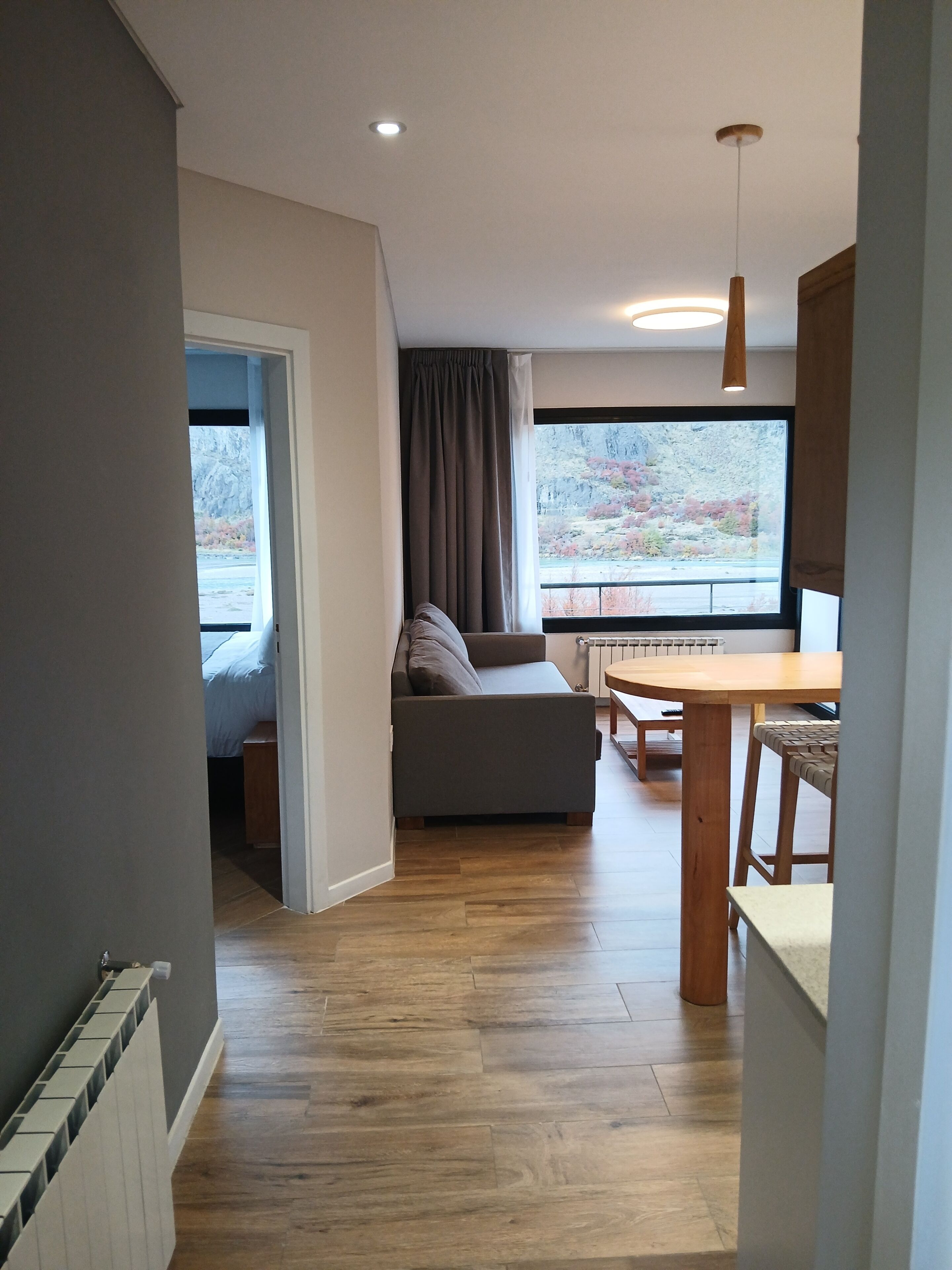 A modern interior with a sofa, dining table, and a view of autumn foliage through a window.