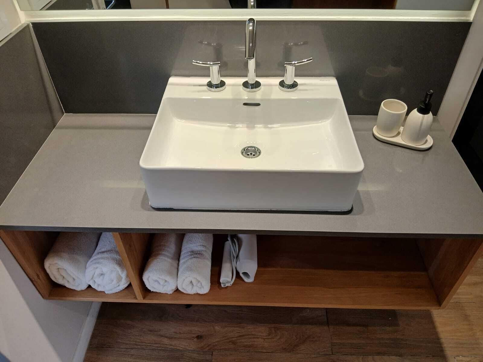 A bathroom with a white sink, two faucets, a soap dispenser, and a towel rack with towels.