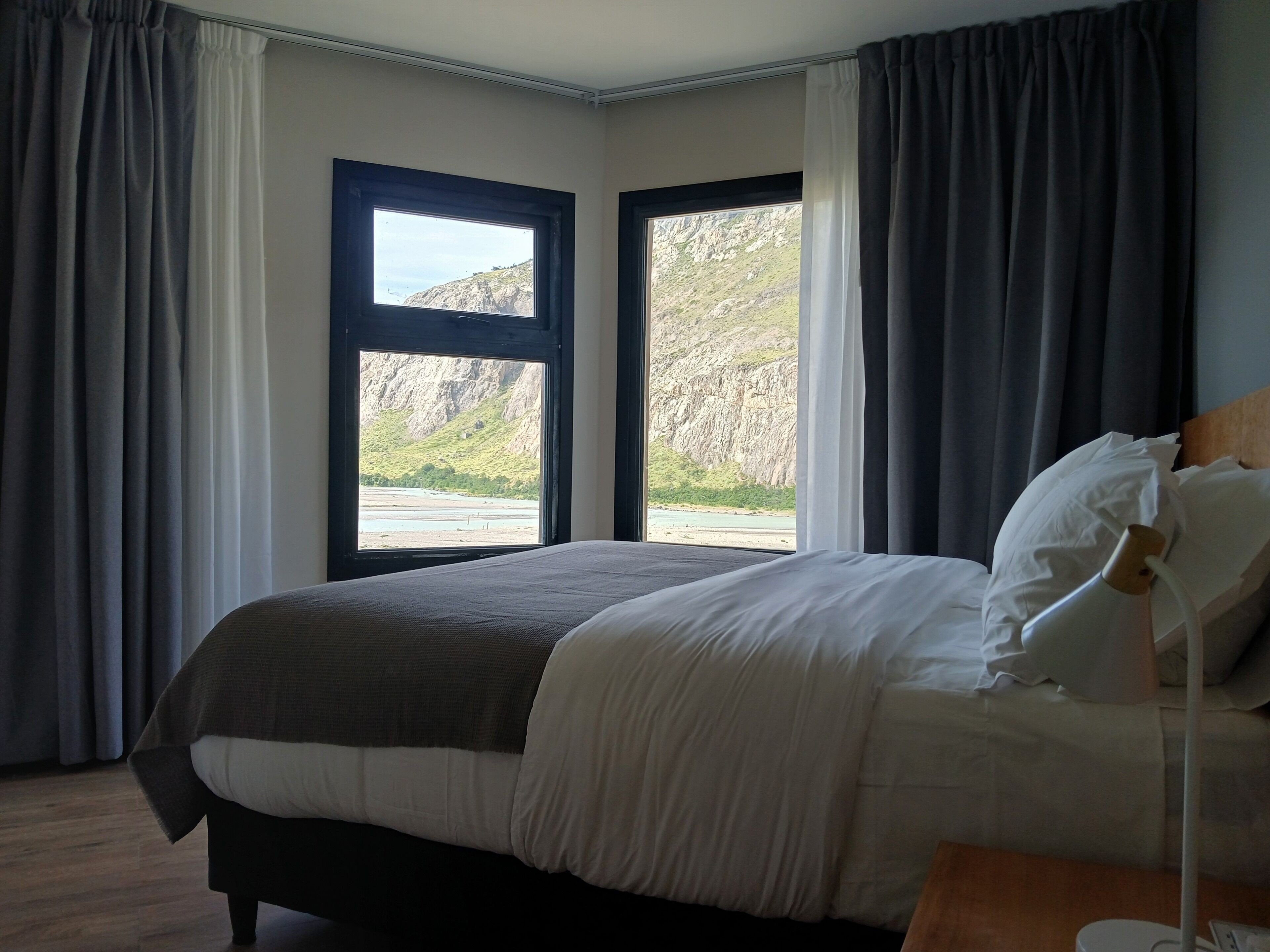 Un dormitorio con cama, mesita de noche y ventana con cortinas.