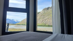 Une chambre avec un lit, deux fenêtres donnant sur la montagne et un rideau.