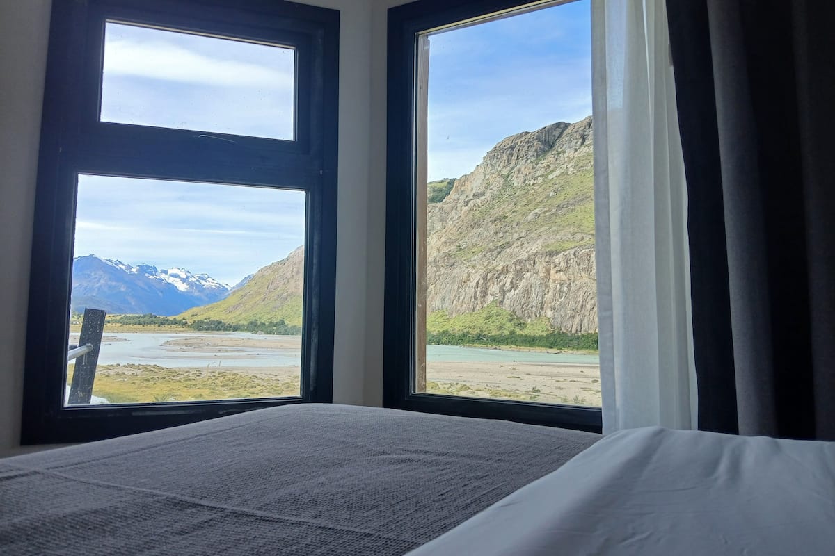 Una stanza con un letto, due finestre vista montagna e una tenda.