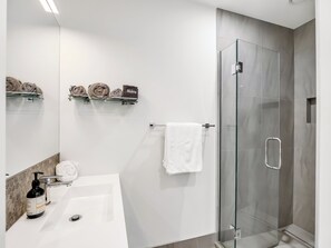 Ein modernes Badezimmer mit einer Glasdusche, einem weißen Waschbecken und einem Spiegel.