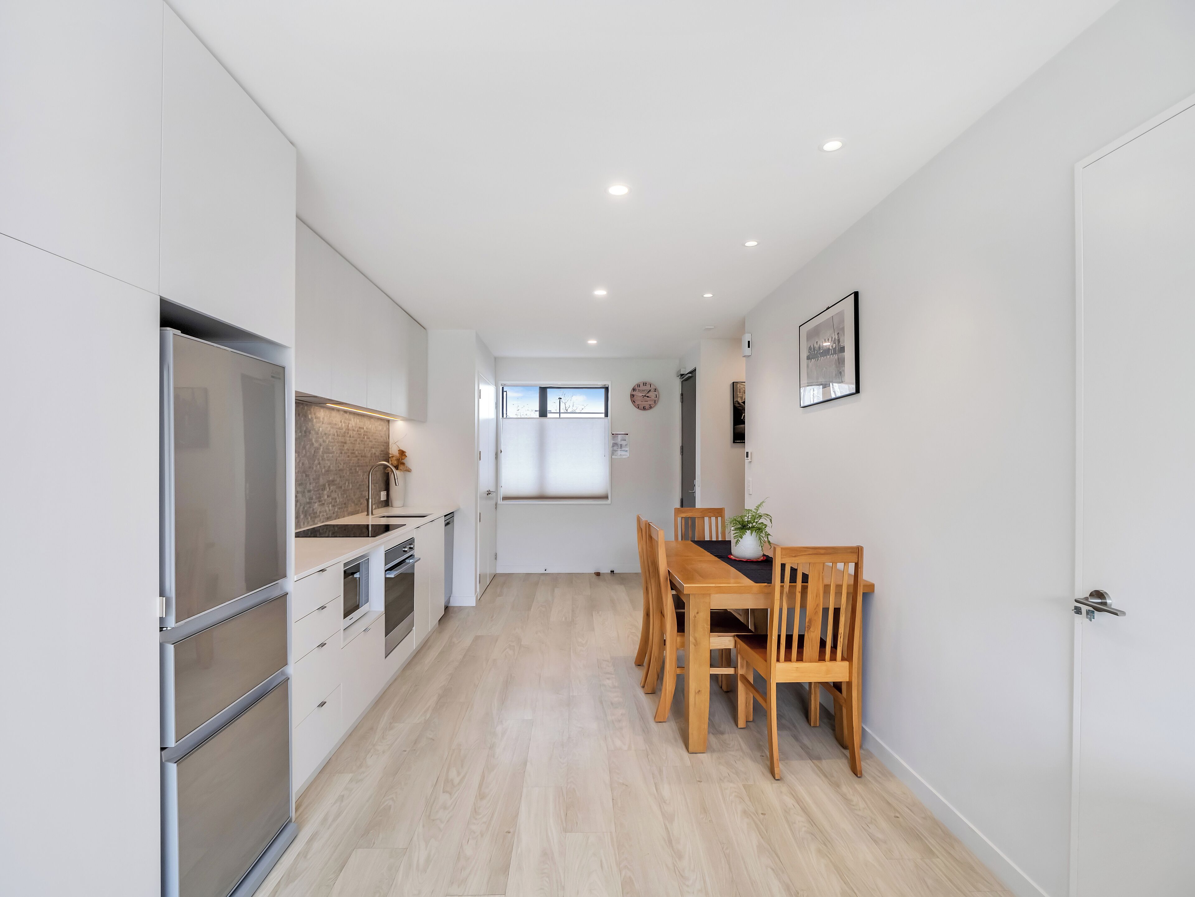 Une cuisine moderne avec des meubles blancs, des appareils en acier inoxydable et une table à manger en bois, assortie de chaises.