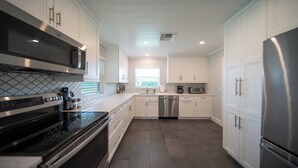 A modern kitchen with stainless steel appliances, white cabinetry, and a patterned backsplash. - Cozy retreat with Modern Comforts (Marco Island)
