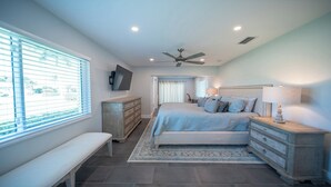 A bedroom with a bed, a bench, a dresser, a TV, and a ceiling fan. - Cozy retreat with Modern Comforts (Marco Island)