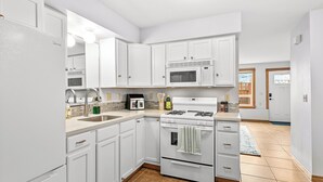 Una cocina moderna con armarios blancos, un microondas integrado, una estufa a gas y un lavamanos.