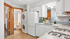Una cocina moderna con armarios blancos, estufa a gas, lavadora y lavavajillas.