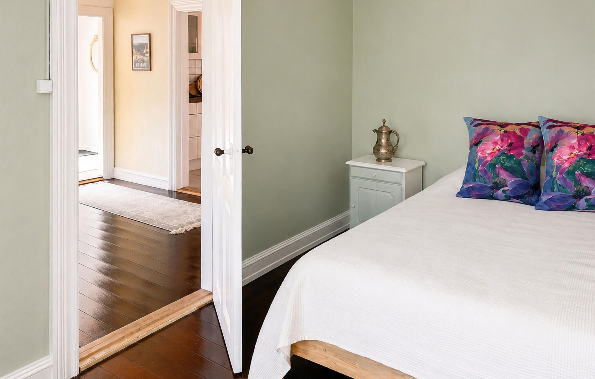 A bedroom with a bed, a nightstand, a lamp, and a door leading to another room.