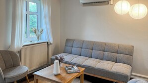 A cozy living room with a grey sofa, a wooden coffee table, and a window with white curtains. - Awesome home in Skagen with WiFi (Skagen)