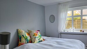 A bedroom with a bed, two colorful pillows, a bedside lamp, a window with curtains, and a view of a wooden fence outside. - Awesome home in Skagen with WiFi (Skagen)