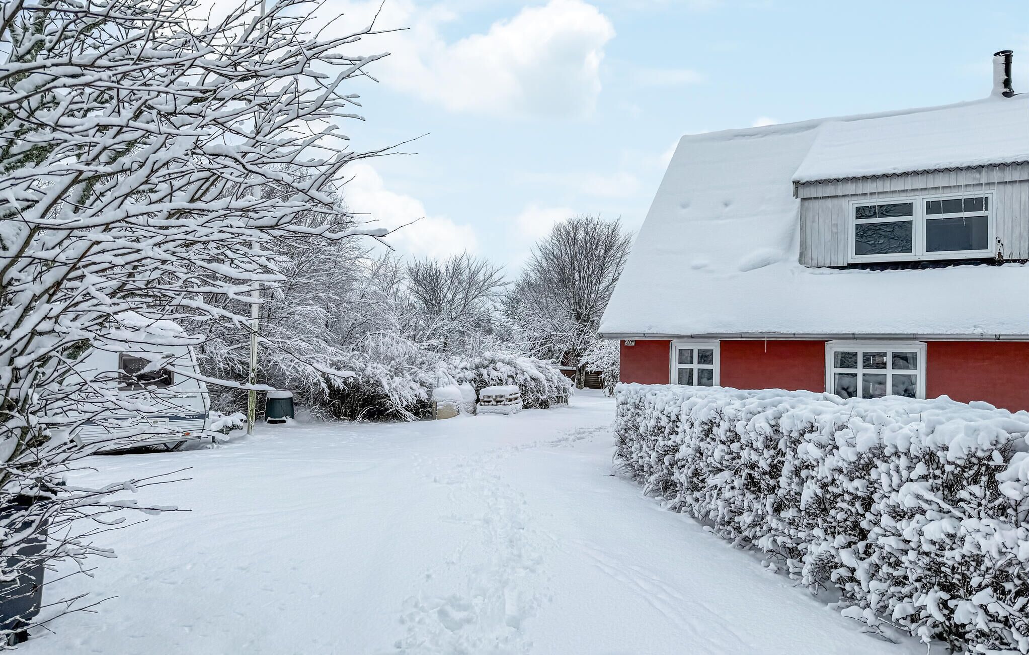 A snow-covered residential area with a red house, a pathway, and snow-laden trees.