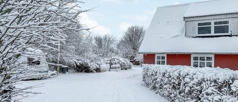 A snow-covered residential area with a red house, a pathway, and snow-laden trees.