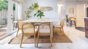 A modern dining area with a white table, wicker chairs, and a potted plant.