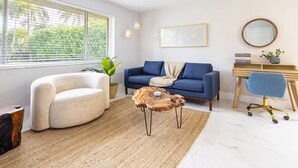 A modern living room with a blue sofa, a white armchair, a wooden coffee table, and a desk with a chair.